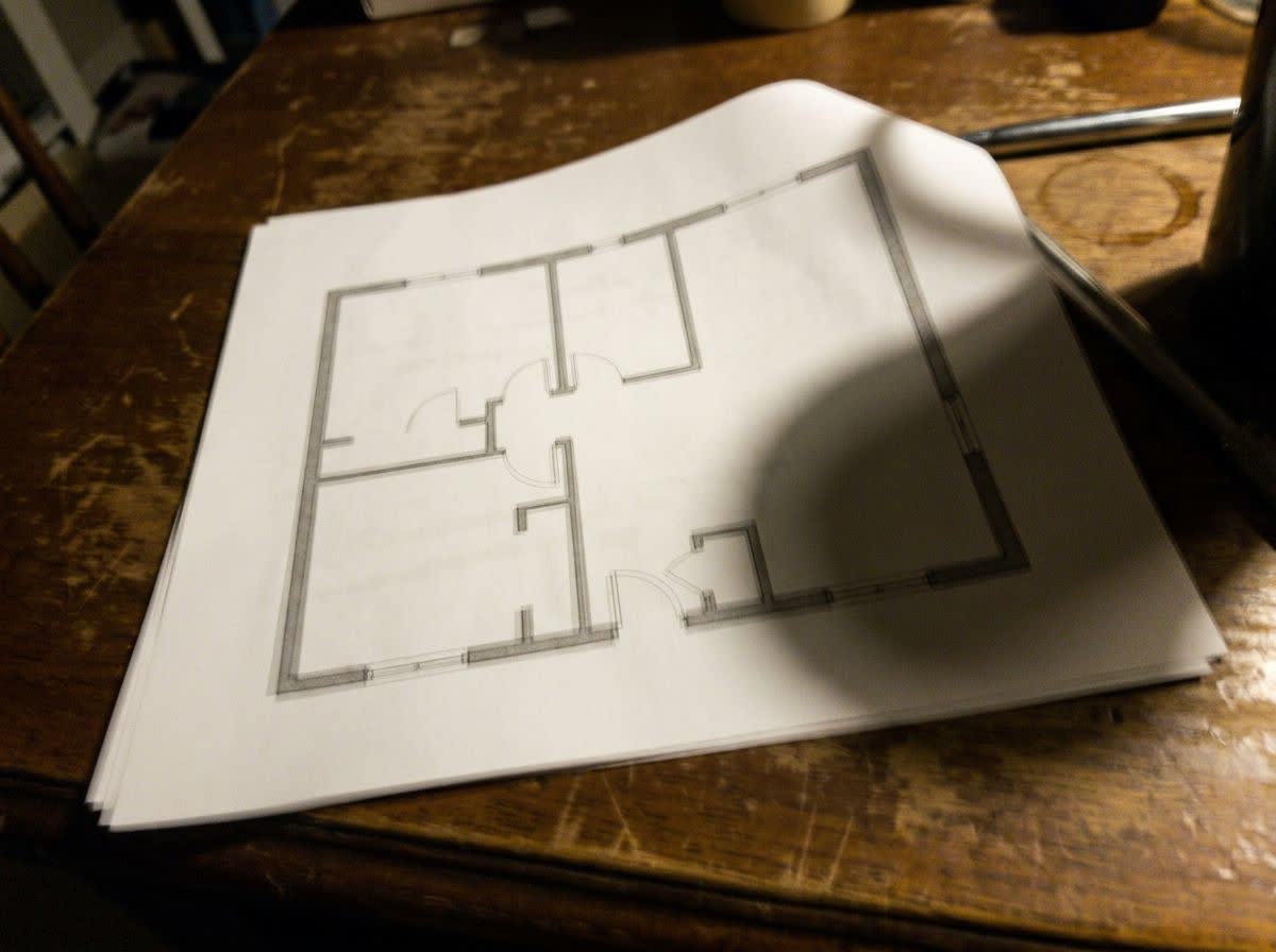 A blurry phone photo of a printed floor plan taken at an angle with a shadow across it