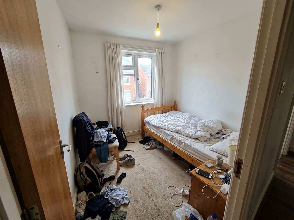 A cluttered small rental bedroom with bare white walls